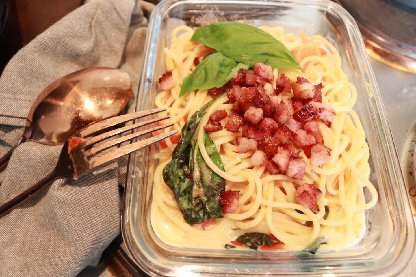 Recette facile de spaghettis au camembert et aux tomates au four Vegan dans un plat à rôtir en verre avec des couverts en cuivre/bronze et un torchon gris.